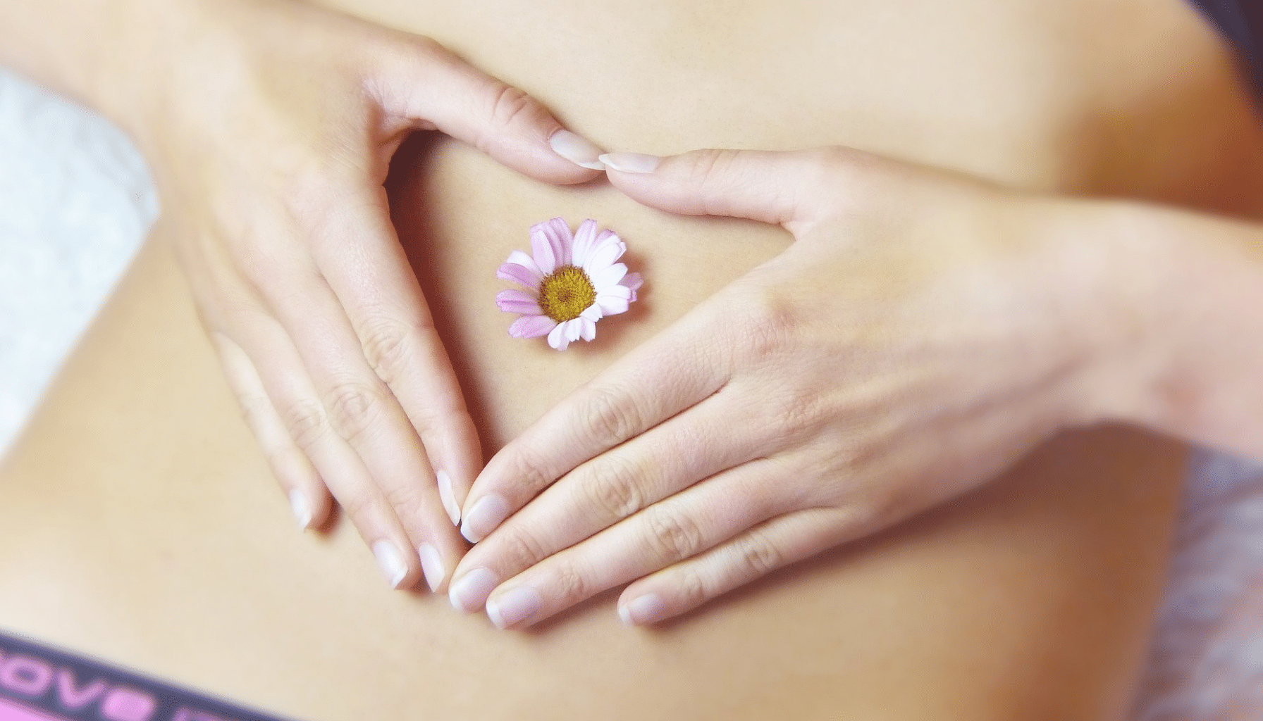 A woman with hands over her belly button and a pink flower.